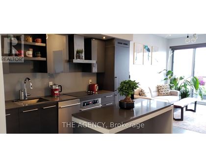 A modern kitchen with a large island and a living area with a couch and plants.