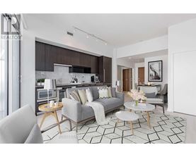 A modern living room with a grey sofa, a coffee table, and a kitchen area in the background.