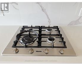 A gas stove with a silver finish and black knobs is on a marble countertop.