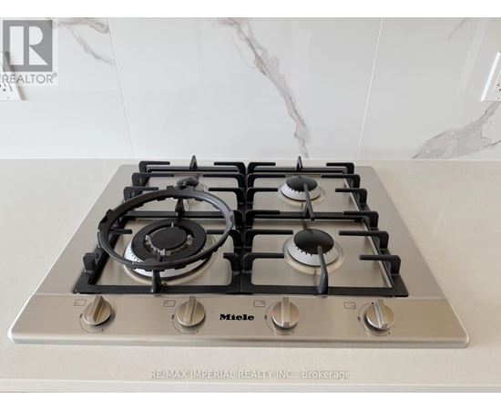 A gas stove with a silver finish and black knobs is on a marble countertop.