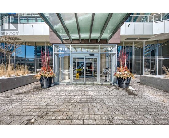 The image shows the front of a REALTOR® building with a glass entrance and two large planters with red plants.