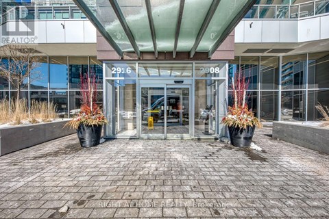 The image shows the front of a REALTOR® building with a glass entrance and two large planters with red plants.