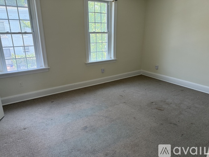 A room with a carpeted floor and two windows.