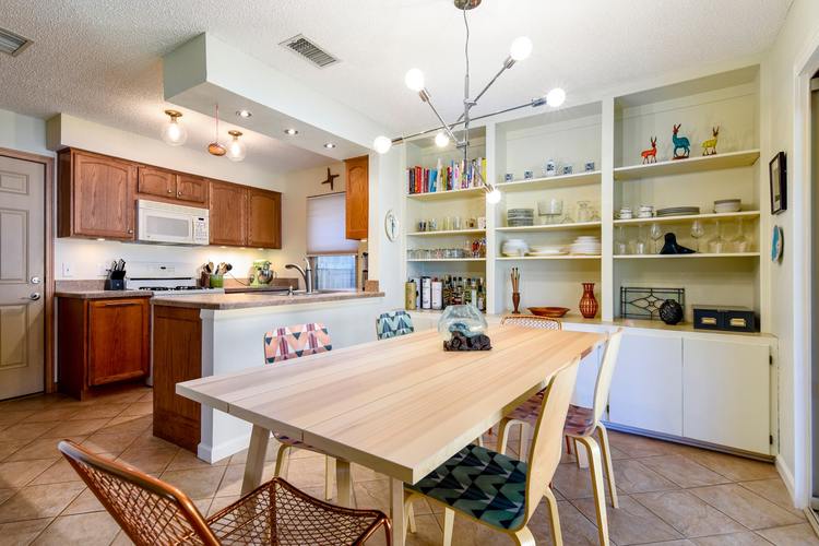 A kitchen with a table and chairs in the foreground and a shelf with various items on it in the background.