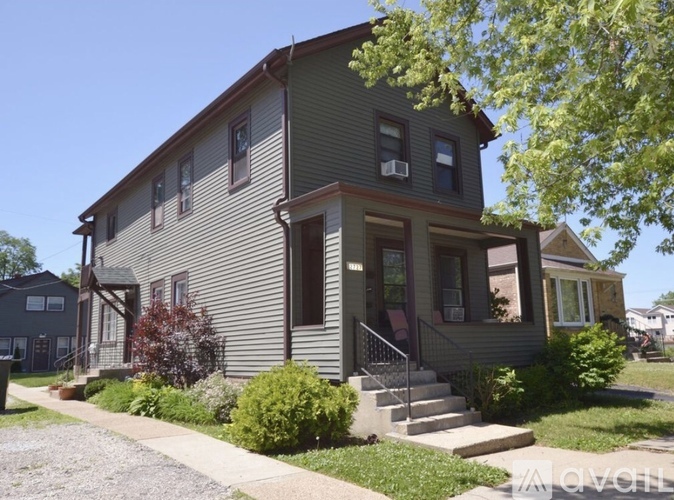 A house with a grey siding and a red door is surrounded by greenery.