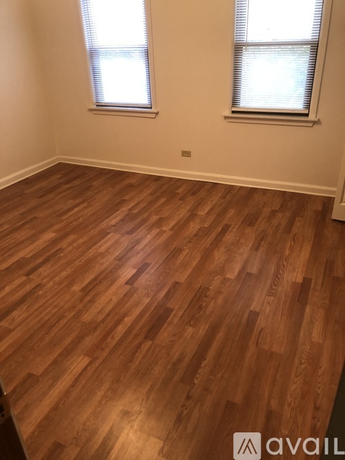 A room with wooden flooring and two windows.