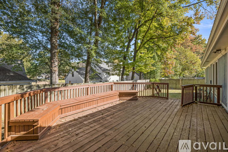 A wooden deck with a railing and a bench is surrounded by trees.
