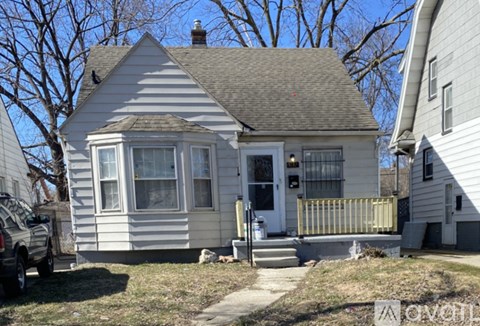 A small white house with a grey roof and a car parked in front.