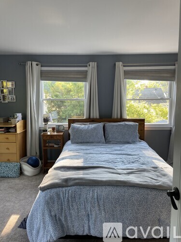 A bedroom with a bed, nightstand, and window with curtains.