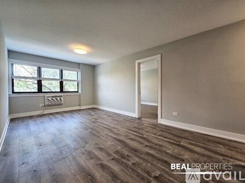A spacious room with wooden flooring and a window with blinds.