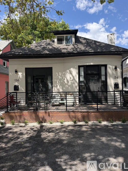 A white house with black shutters and a black roof with a balcony in front.