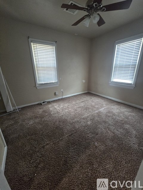 A room with a carpeted floor and two windows.