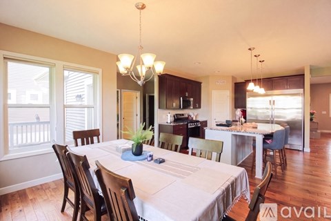 A dining room with a table set for six with a white tablecloth and a chandelier hanging from the ceiling.