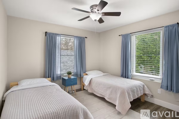 A bedroom with two beds, a ceiling fan, and a window with blue curtains.