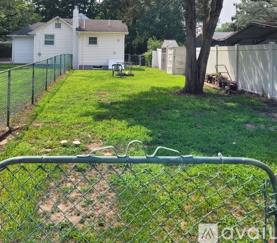 A chain link fence surrounds a yard with a white house in the background.