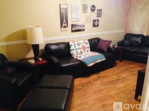 A living room with black leather furniture and a wooden floor.