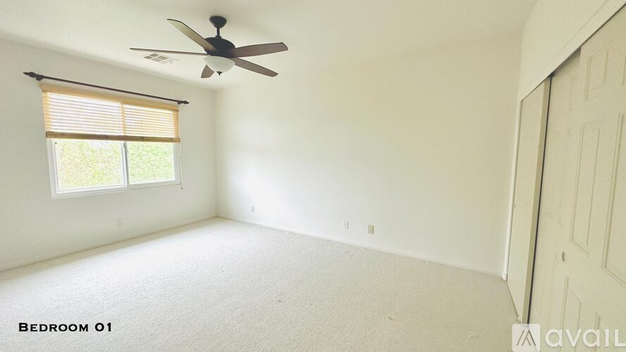 A spacious bedroom with a ceiling fan and a window with blinds.
