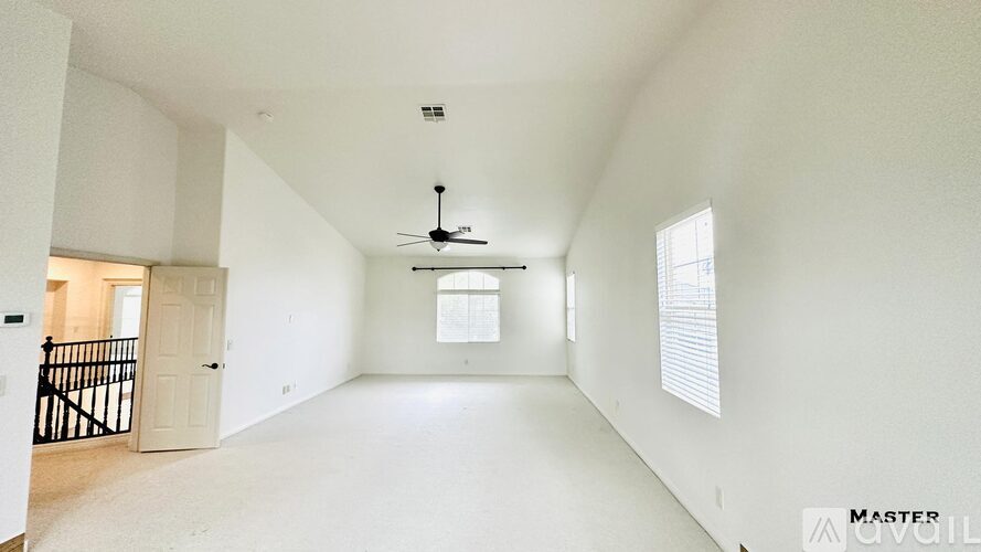 A spacious, empty room with white walls and a ceiling fan.
