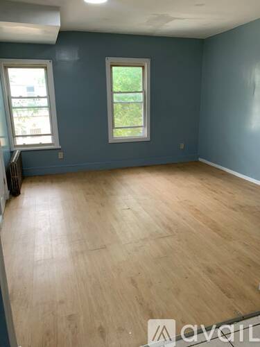 A room with wooden flooring and two windows.