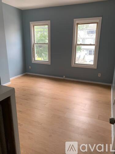 A room with wooden flooring and two windows.