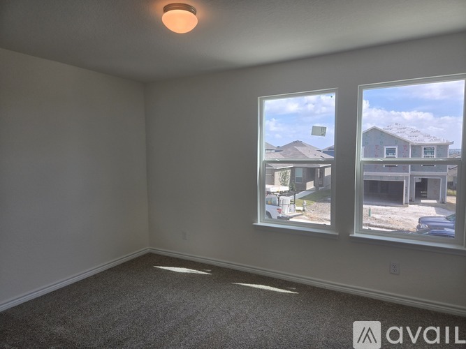 A room with a carpeted floor and two windows showing a view of houses and trees.