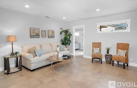 A living room with a white couch, two chairs, and a table with a lamp.