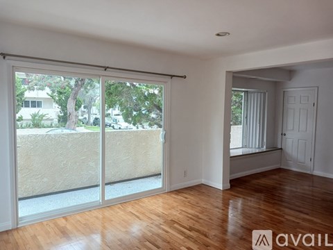 A room with wooden floors and a sliding glass door leading to a balcony.