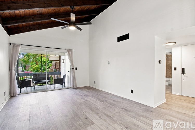 A spacious room with a ceiling fan and a sliding glass door leading to a balcony.