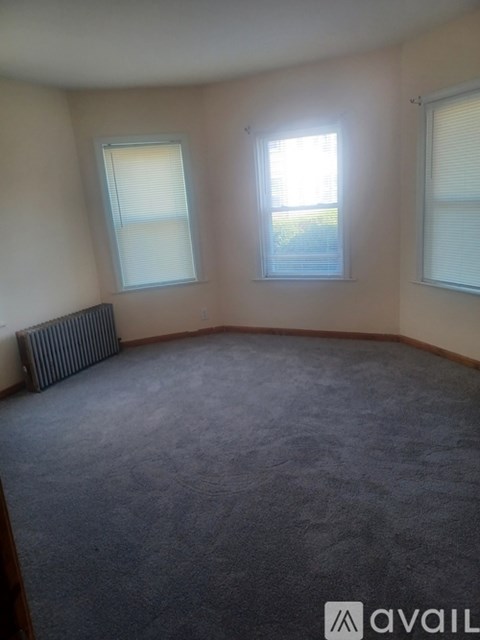 A room with a carpeted floor, a window with blinds, and a radiator.