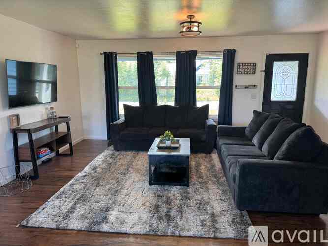 A living room with a black couch and a rug.