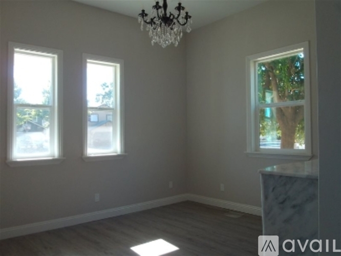 A room with a chandelier, two windows, and a view of trees outside.