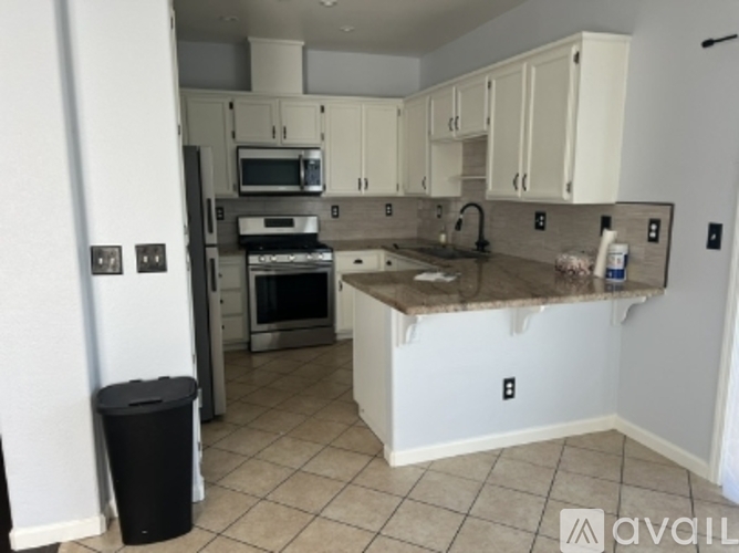 A kitchen with white cabinets and a black trash can.