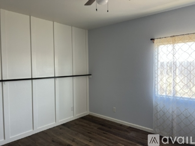 A room with a window covered by a white curtain and a fan on the ceiling.