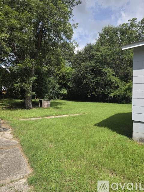 A grassy area with a tree stump and a house in the background.