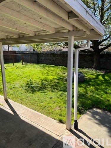 A white pergola over a concrete walkway with a green lawn in the background.