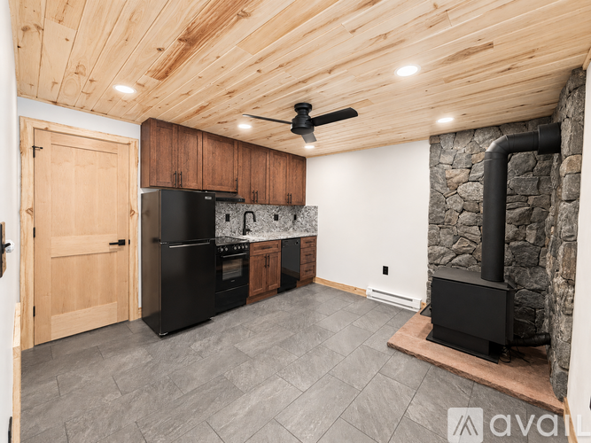 A kitchen with a black refrigerator and stove, a ceiling fan, and a stone fireplace.
