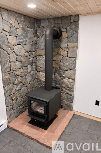 A black wood stove with a tall chimney is in front of a stone wall.