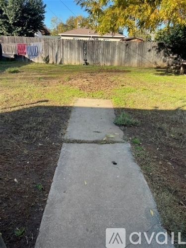 A concrete pathway leads to a grassy area with a wooden fence and a house in the background.