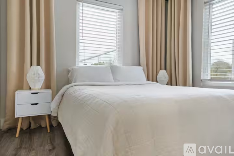 A bedroom with a large bed, a nightstand with a lamp, and a window with curtains.