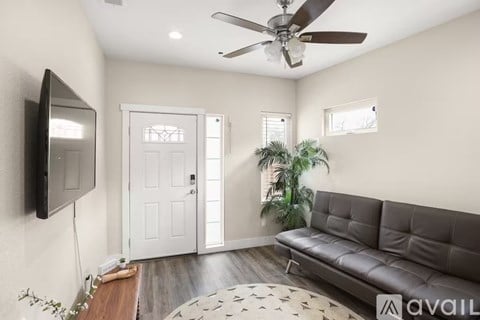 A living room with a grey sofa, a flat screen TV, a ceiling fan, and a wooden floor.