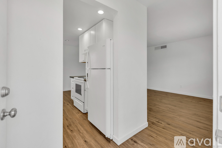 A white refrigerator is in a kitchen with wood flooring.