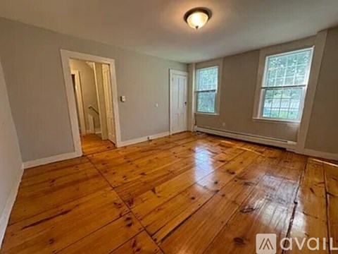 A room with wooden flooring and two windows.