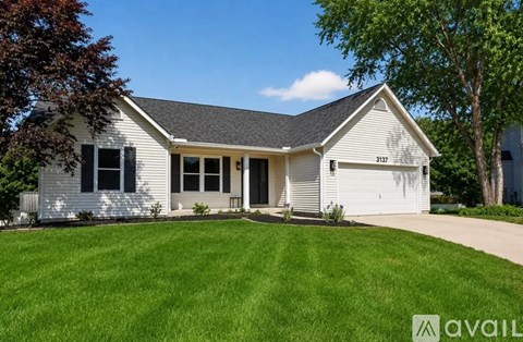 A house with a white exterior and a grey roof is surrounded by a green lawn.
