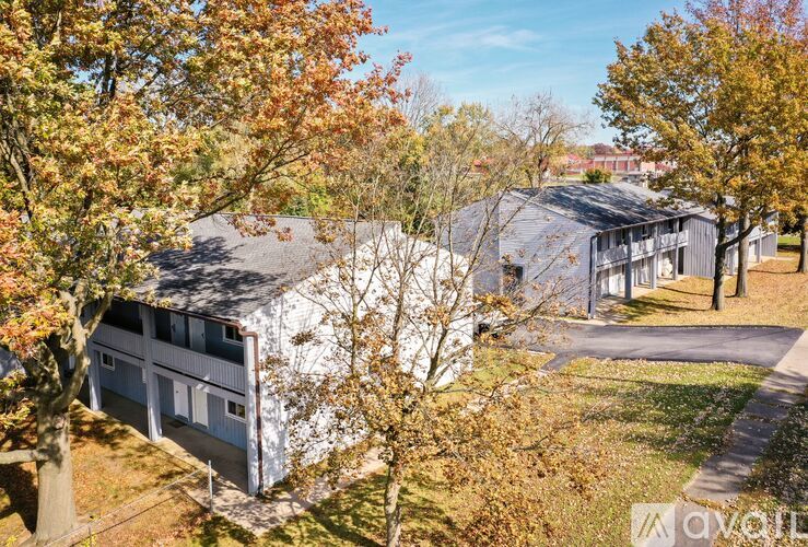 A white barn-like building is surrounded by trees with autumn leaves.
