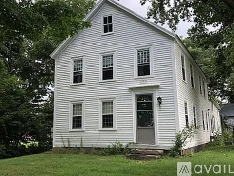 A white house with a grey door and windows surrounded by trees.