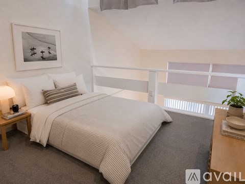 A bedroom with a large bed and a small table with a lamp on it.
