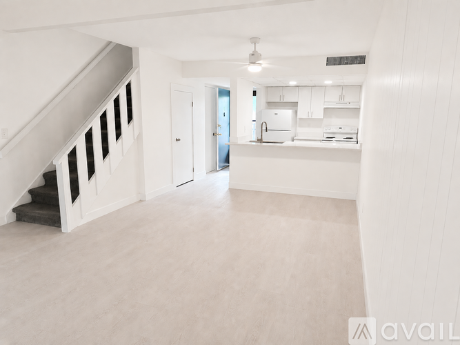 A spacious, empty room with a staircase on the left and a kitchen area in the background.