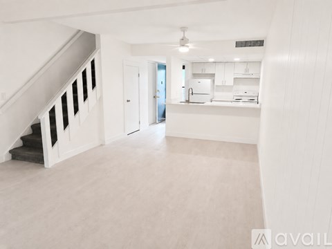 A spacious, empty room with a staircase on the left and a kitchen area in the background.