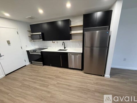 A kitchen with black cabinets and a stainless steel refrigerator.