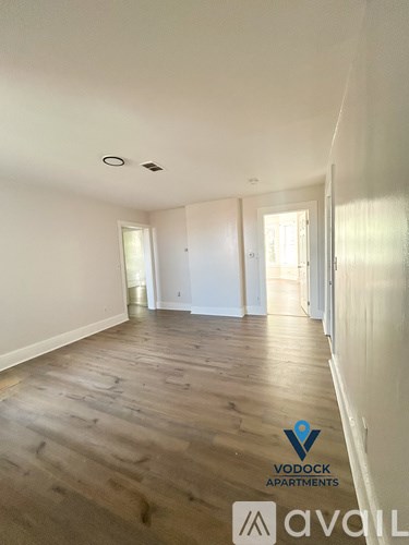 A spacious room with wooden flooring and white walls, with a logo for Vodock Apartments in the corner.